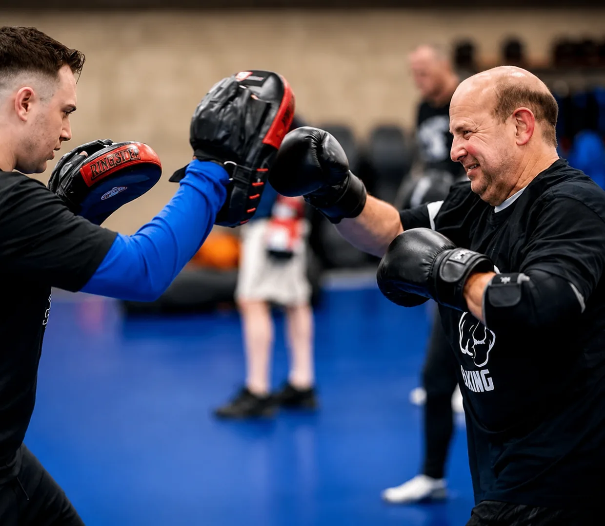 Coach Dean Moskowitz holding focus mitts while a member throws a punch during pad training