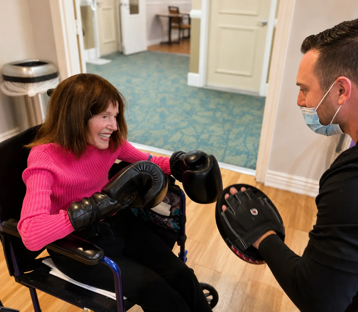Coach Dean holding a focus mitt while a seated client in a wheelchair throws a punch during one-on-one training