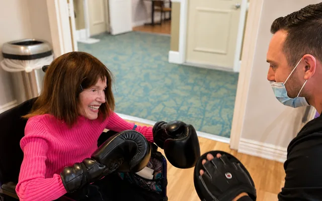 Coach Dean holding a focus mitt while a seated client in a wheelchair throws a punch during one-on-one training